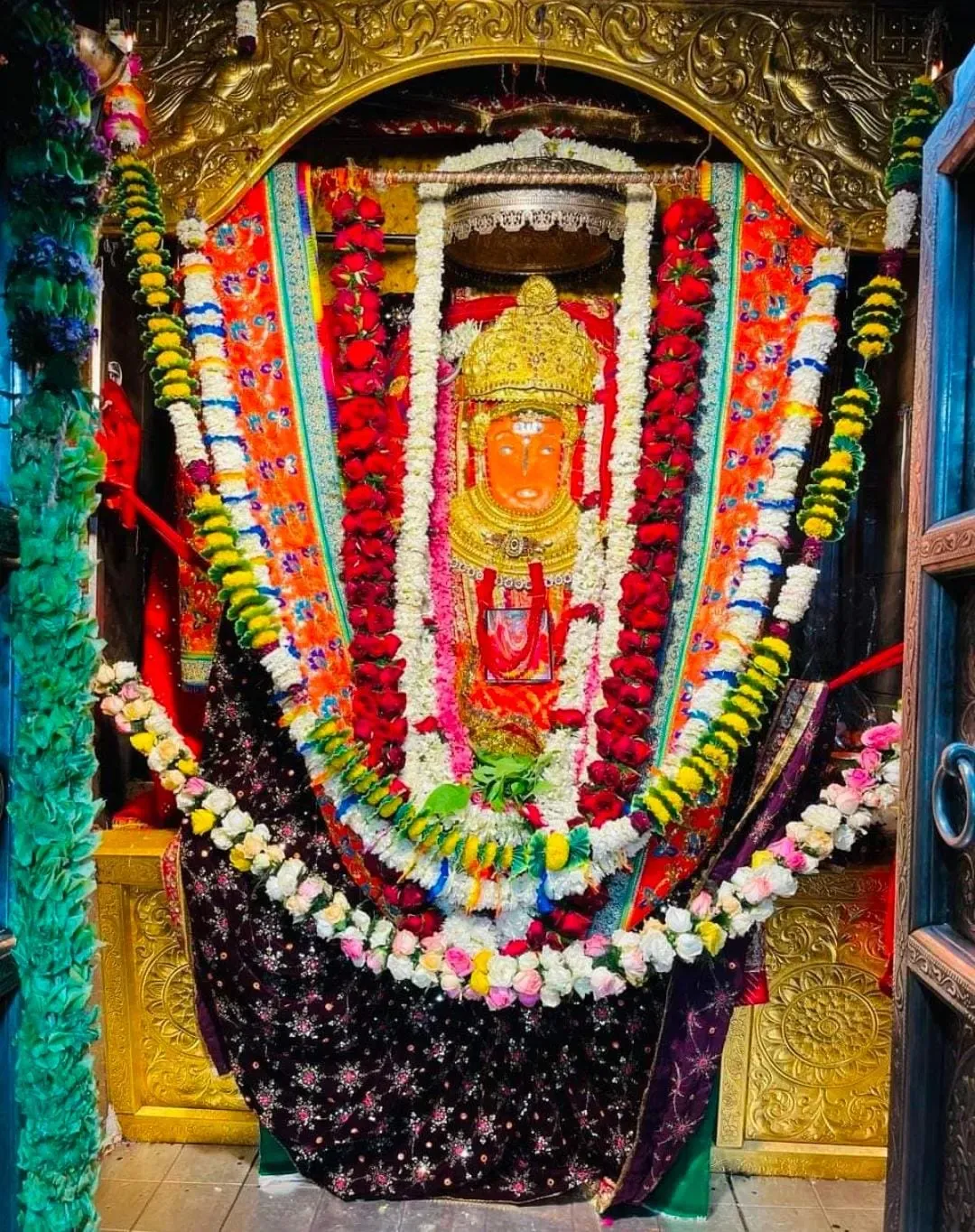 Jeen Mata in the sanctum, her sindoor-orange face crowned in gold and framed by garlands of roses, marigold and white flowers